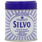The image depicts the packaging of Reckitt Benckiser Group plc Cleaning and Maintenance Silvo Tarnish Guard Polish Wadding, with a weight of 75G. The product appears to be a creamy, waxy substance in a round container, with the Silvo logo prominently displayed. The background features a shiny surface with a tarnished area, suggesting the products use in removing tarnish from metal surfaces.