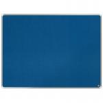 The photograph shows a blue Nobo Premium Plus Felt Notice Board by ACCO Brands. The board has a dimension of 1200x900mm, making it a large and spacious notice board. Its high-quality felt material gives it a professional and sleek appearance. The edges are neatly trimmed, and the surface is smooth and even. The board is mounted on a wall, and a few pages of important documents are pinned onto it with colorful push pins. The lighting in the room reflects off the board, adding a slight shine to the surface. The overall aesthetic is clean and organized, perfect for displaying important information or announcements.