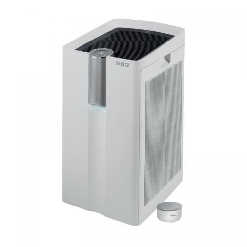 This photo shows a sleek, modern Leitz TruSens™ Z-6000 Performance Series Air Purifier with a E12 EPA combination carbon filter and a remote SensorPod™. The purifier is in a clean, well-lit room and is emitting a soft blue light. Its compact size makes it a convenient addition to any space.