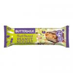 Image shows a wrapped Buttermilk Plant Powered peanut nougat caramel bar beside a cut-open piece. Cream-and-brown wrapper rests next to a glossy chocolate-coated bar, revealing sticky caramel, pale nougat layers and scattered roasted peanuts.