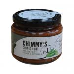 Six 200g jars of Chimmy’s Chimichurri Traditional sit in a neat row, their glass revealing vibrant emerald-green sauce flecked with parsley, garlic and chili. Clean white labels show the brand logo; light catches an oily sheen. A rustic wooden surface and soft shadows frame them. With flecks on lids