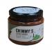 Six 200g jars of Chimmy’s Chimichurri Traditional sit in a neat row, their glass revealing vibrant emerald-green sauce flecked with parsley, garlic and chili. Clean white labels show the brand logo; light catches an oily sheen. A rustic wooden surface and soft shadows frame them. With flecks on lids
