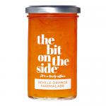 Six glass jars of The Bit on the Side Seville Orange Marmalade sit in a neat row, amber preserve and suspended peel visible through clear glass. Each jar has a white label with bold black logo and a black lid. Warm studio light highlights glossy texture and subtle reflections. On a wooden surface lit.