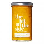 Six identical glass jars sit in a neat pack, each filled with bright yellow chunky piccalilli with visible cauliflower and vegetable pieces. Paper labels show 'The Bit on the Side' and 'Sweet Piccalilli'. Metal lids reflect light on a plain white background.