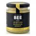 A clear glass jar of golden Scottish blossom honey sits on a plain surface, its label bearing The Scottish Bee Company name and product title in neat type. Six identical jars are arranged in two rows; light catches the viscous honey and a wooden dipper leans against one jar. Subtle shadows surround.