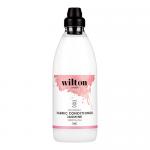 Six upright 1L bottles stand in orderly rows, white plastic with green caps and branded front labels. Labels display the Wilton London name, jasmine floral artwork, eco graphics and product text. Soft studio lighting casts subtle reflections on a neutral background. One bottle leans slightly forward