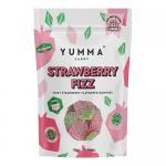 Seven bright pink Yumma candy pouches fan across a white background, each glossy pouch showing a large strawberry illustration, effervescent fizz bubbles and scattered red candy pieces. The bold Yumma logo and playful typography stand out on each pouch Soft reflections and faint creases add texture