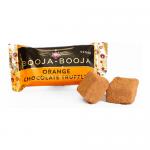 A small two-truffle pack sits against a white background, its orange-accented sleeve featuring brown lettering. Two glossy chocolate truffles rest beside the box, one halved to reveal a soft, orangey center and a smooth ganache interior dusted with cocoa.