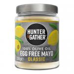 A row of containers fills the frame: a white 250g tub of Hunter & Gather Egg Free Classic Olive Oil Mayo with a green-and-white label sits beside six assorted chutney and condiment jars in glass and plastic, their colorful labels and sauces creating a clustered, shelf-ready arrangement and shadows.