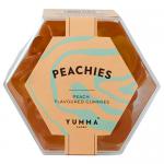 A hexagonal clear plastic tub shows glossy peach-colored gummy hexagons stacked neatly. A bright peach-and-white label with playful Yumma logo wraps the side, accented by illustrated peach slices and subtle sparkle highlights. Lighting emphasizes chewy, translucent texture. With a pale, glossy sheen.