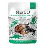 A small matte pouch displays the Nalo logo and smoked-rosemary labeling. A clear window shows golden-brown almonds dusted with herb flakes. Rosemary sprigs and salt crystals scatter across the foreground on a simple neutral background, with earthy green and amber tones. A soft shadow grounds the pack.