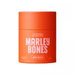 Six slim 90g packs sit in a neat row, each bearing Marleybones branding and a cheerful dog illustration. Clear windows reveal golden-brown soft-baked chews. Packaging uses bright green, white and orange accents with small icons and product text.