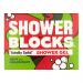 Six solid shower blocks sit arranged on a wooden tray and in open cardboard box, alternating mint-green and coral-pink bars. Fresh mint leaves and halved grapefruit rest beside them on wet ceramic tile, with soft natural light and water droplets highlighting textures. Soft reflections on glossy edges