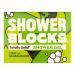 Six compact lime-green solid shower blocks rest on a wooden tray, grouped with fresh lime halves and slender sandalwood sticks. Water droplets bead on textured surfaces under soft natural light, set against neutral ceramic tiles and a folded beige towel in the background. Soft, low shadows surround.