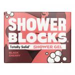 Six deep-red solid shower gel blocks sit stacked on a wooden tray, their glossy surfaces dotted with water droplets. A black cherry slice and green leaves rest nearby, while soft natural light highlights textured ceramic tiles and a chrome showerhead in the blurred background. Subtle sheen glimmers.
