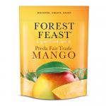 A clear front pouch displays bright orange dried mango slices alongside glossy almonds, pumpkin seeds and sunflower kernels. A simple matte label at top shows the brand name and product title in green lettering, with nutritional icons and a small weight indicator. The backdrop is a pale wood surface.