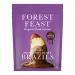 Image shows a glossy Belgian milk chocolate slab studded with whole Brazil nuts and a scatter of dried fruits, nuts and seeds. Pieces sit on a textured wooden board beside a minimalist wrapper bearing Forest Feast branding.