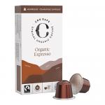 A rectangular retail box sits upright, showing a minimalist brown and cream design with a circular CRU Kafe logo at center. Several espresso pods lie beside the box, each with metallic foil lids and ridged plastic bases. Small ingredient and company text appears on the box rear. Soft highlights glint.