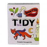 The photograph shows a small rectangular box of Tidy Tea Winter Warmer tea, its snowy blue and deep red packaging featuring winter foliage illustrations and bold product name. A clear window reveals triangular plastic-free pyramid tea bags arranged in neat rows on a white background. Soft steam haze