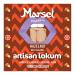 A rectangular Marsel Delights box presents six individually wrapped hazelnut-and-caramel lokum cubes visible through a clear window. Glossy packaging uses warm gold and brown tones, showing caramel swirls, chopped hazelnuts and a light dusting of powdered sugar on each cube. Label shows small logo..