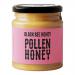 Six glass jars sit in a neat row, filled with amber honey and flecks of pollen. Labels feature a stylized black bee and British flag motifs in black and gold. Metal screw lids reflect light. A simple white background emphasizes the warm, glossy texture of the honey. Soft shadows add warmth and depth.