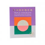 The photo shows a 75g Chococo milk chocolate bar (47% Colombia) partially unwrapped, revealing a glossy, creamy milk slab studded with dark and white chocolate chips; several wrapped bars and a stacked pack of twelve sit behind on a neutral surface. Soft reflections highlight the creamy texture now.