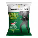 A Savoursmiths crisps bag sits on a plain backdrop, its colorful packaging displaying the brand name, an illustration of golden, ridged crisps spilling out, a chunk of Somerset cheddar and a sliced shallot with green garnish, lit by even studio lighting. Soft shadows fall around the bag. Soft sheen.