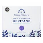 A photo shows eight round chocolate discs wrapped in glossed dark foil with pale mint-green labels stamped with the Summerdown Heritage name. Some discs stack while others lie flat, revealing slightly ridged surfaces and tiny white peppermint flecks that catch soft studio light. A small branded box.