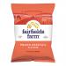A glossy Fairfields Farm crisp bag stands upright, labeled Prawn Cocktail with 150g shown on the front. Warm pink and coral tones surround an illustration of prawns and scattered potato crisps. The brand logo appears above a detailed close-up of crunchy chip texture. Soft studio light adds warm sheen.