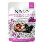 A compact bright packet features the Nalo logo and bold product name, with a transparent window revealing roasted cashews and almonds speckled with black pepper and salt crystals. A minimalist background highlights the textured nuts and glossy snack packaging. The foil seams catch light subtly nearby