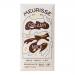 Photo shows a Meurisse milk chocolate display: several 100g bars stacked beside an unwrapped bar with glossy, ribbed segments and a smooth, creamy milk filling exposed. The wrapper lies folded back, showing the brand name and soft, warm tones against a neutral background. Soft light accents texture.