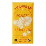 A Meurisse milk chocolate bar in 100g packaging sits on a neutral surface. Smooth, glossy brown chocolate snaps to reveal roasted hazelnut halves and pieces embedded throughout. The wrapper features warm brown and cream branding with a clear window showing the nut-studded bar. Soft highlights shine.