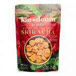 A colorful display shows a box of Kin & Deum Sriracha rice chips with twelve individual 60 g packs arranged around it. Bright red and white packaging features the Kin & Deum logo, chili graphics, and crisp rice chip images against a clean white background. Scattered chips and chili flakes lie nearby.