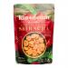 A colorful display shows a box of Kin & Deum Sriracha rice chips with twelve individual 60 g packs arranged around it. Bright red and white packaging features the Kin & Deum logo, chili graphics, and crisp rice chip images against a clean white background. Scattered chips and chili flakes lie nearby.