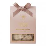 A rectangular glossy box in warm cream and honey-gold tones displays artisanal nougat pieces studded with whole macadamias. A clear window reveals textured white nougat; elegant script branding, delicate floral accents and a honey-drip illustration complete the refined packaging. Soft halo frames it