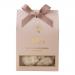 A rectangular glossy box in warm cream and honey-gold tones displays artisanal nougat pieces studded with whole macadamias. A clear window reveals textured white nougat; elegant script branding, delicate floral accents and a honey-drip illustration complete the refined packaging. Soft halo frames it
