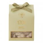 A rectangular box of roasted almond honey nougat features warm cream and gold packaging with a photo of glossy almond-studded nougat pieces. Elegant script and subtle floral accents frame the image.