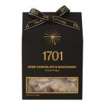 A sleek dark brown box features glossy images of rectangular nougat pieces enrobed in dark chocolate, scattered macadamia halves and a honey drizzle. Warm gold lettering and minimalist graphics frame the confection photos against a matte background. Subtle embossing and ribbon band add warm texture.