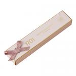 Wrapped in glossy gold and cream paper, the Macadamia Honey Nougat Bar sits diagonally on a dark slate surface. A torn corner reveals pale nougat studded with whole macadamia nuts and a drizzle of amber honey, while soft shadows create warm, textured contrast. Soft crumbs and tiny reflections glint.