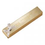 A rectangular nougat bar sits unwrapped, its pale honey-colored interior studded with halved macadamias and amber caramel brittle shards. A glossy caramel drizzle and scattered sea-salt crystals contrast with the soft, chewy nougat texture and toasted nut flecks.