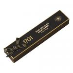A stack of glossy dark-brown wrappers with gold trim shows macadamia nuts and honey illustrations. One bar sits unwrapped and sliced, revealing dense amber nougat studded with whole macadamias and enrobed in glossy dark chocolate that gleams under soft light.