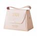 A small handbag-shaped box in warm cream and honey tones sits against a white background. A clear window reveals pale nougat studded with macadamia halves and amber honey swirls; gold lettering and a ribbon handle finish the packaging.
