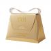 A handbag-shaped tin with a glossy caramel-brown exterior, embossed lettering and a tied ribbon. The lid opens to reveal golden salted caramel brittle and pale macadamia honey nougat pieces studded with glossy nuts, set against a crinkled paper liner.