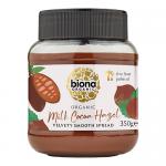 Six glass jars of Biona Organic Milk Cocoa Hazelnut spread sit together, each showing a white-and-green label, silver lids and dark glossy chocolate-brown spread visible through the glass. Clean studio lighting highlights texture and subtle swirls on the surface. Background is a neutral white backdrop.