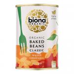 A line of metal cans shows Biona Organic Classic Baked Beans with green-and-white labels marked 400g, stacked on a shelf. The label features baked-bean imagery, organic certification and ingredient text. Soft lighting creates highlights and subtle reflections on curved tin surfaces. Nearby tags blur.