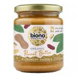 Six glass jars of Biona Organic Crunchy Salted Peanut Butter sit in neat rows. Cream labels display a green Biona logo and product name. Through clear glass the chunky, golden-brown peanut spread and individual peanut pieces are visible; metal lids and soft shadows sit on a white backdrop. Close-up.