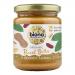 Six glass jars of Biona Organic Crunchy Salted Peanut Butter sit in neat rows. Cream labels display a green Biona logo and product name. Through clear glass the chunky, golden-brown peanut spread and individual peanut pieces are visible; metal lids and soft shadows sit on a white backdrop. Close-up.