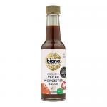 A row of six 140ml glass bottles of Biona Organic Worcester Sauce stands against a plain white background. Each bottle holds dark brown liquid, capped with black lids and wrapped in cream labels showing the Biona logo, product name and ingredient details. A faint reflection glints along each bottle.