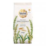 A clear window reveals tightly coiled white spelt fusilli spirals, pale ivory and slightly translucent. A kraft-style carton displays Biona Organic branding, the product name and weight, earthy illustrations and a visible nutritional panel on the back. Soft side lighting accentuates spiral textures.