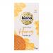 Bright rectangular box displays the Biona Organic logo and green accents. A stack of golden honey-coated waffles sits in the foreground with a glossy honey drip and honeycomb motifs. Organic certificate marks and ingredient illustrations appear on a clean white background. Soft shadow beneath edges.